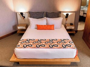 A neatly made bed with a patterned bedspread, two bedside tables with lamps, and a mirror on one of the tables.