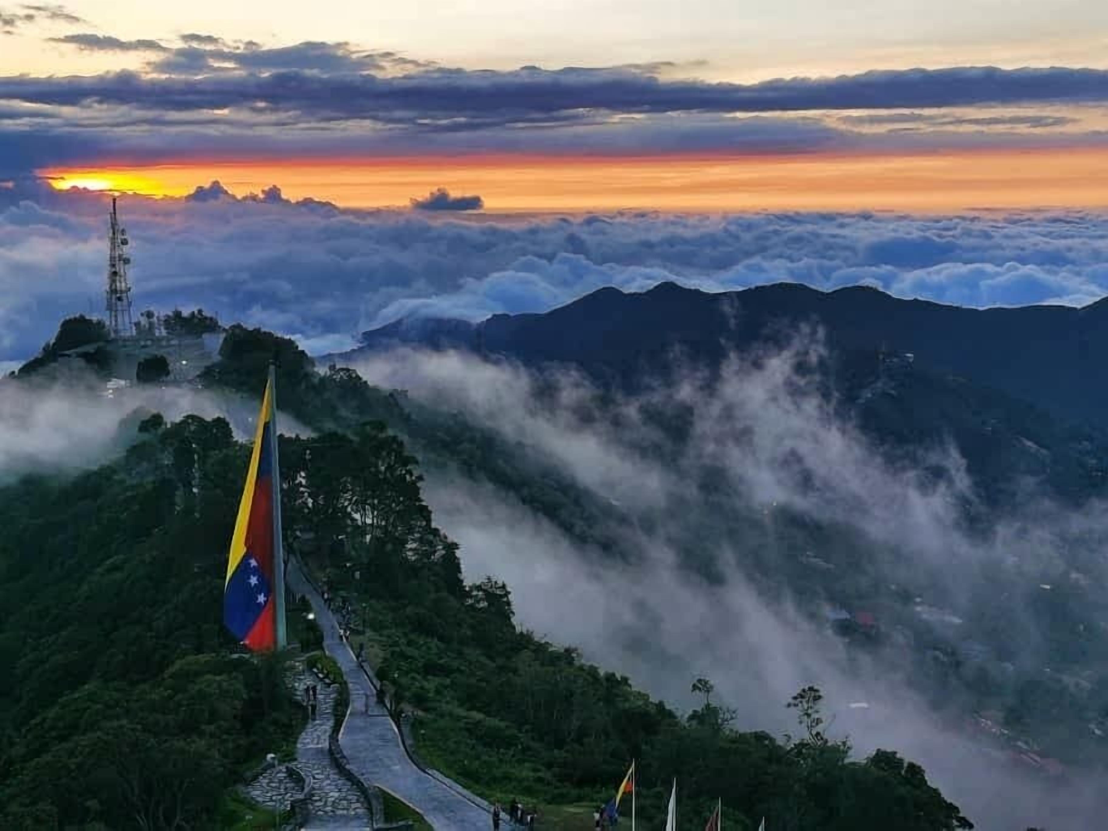 Un paisaje montañoso con un asta de bandera, un sendero y una torre de telecomunicaciones.