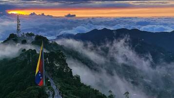 Un paisaje montañoso con un asta de bandera, un sendero y una torre de telecomunicaciones.