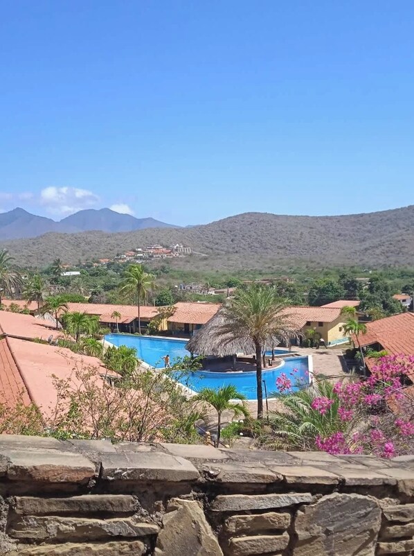 A resort with multiple swimming pools, surrounded by palm trees and a mountainous backdrop.