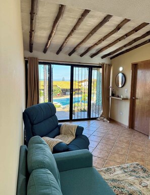 A living room with a sofa, a chair, and a view of a pool and landscape through large glass doors. - Apartamento familiar con piscina en Pampatar (Pampatar)