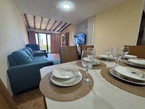 Un comedor con una mesa dispuesta para cuatro personas, un sofá y un televisor al fondo.