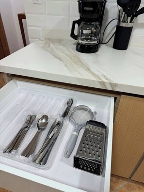 Eine Küchenarbeitsplatte mit einer Kaffeemaschine und einer Schublade mit Besteck und einer Reibe.