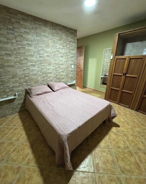 Ein Schlafzimmer mit Bett, Kleiderschrank und einer Steinwand.