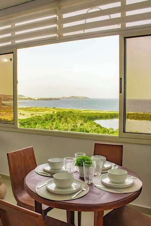 Mesa de jantar posta para quatro pessoas, com vista para a paisagem costeira através de grandes janelas.