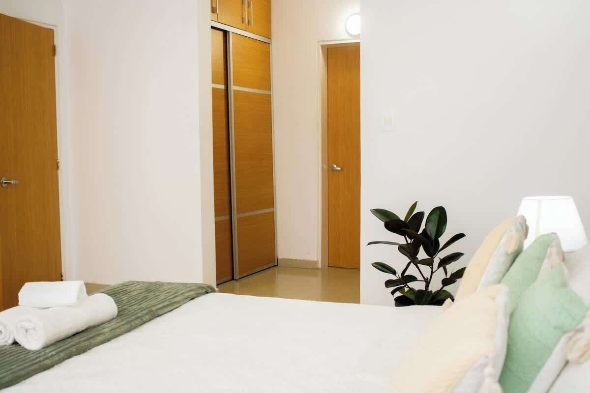 Hotellihuone, jossa on sänky, vihreä matto, kasvi ja vaatekaappi.