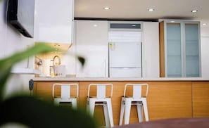 A modern kitchen with white cabinets, a built-in oven, and a refrigerator. There are three white bar stools in front of the counter. - Ocean Blue/ Vista y Atardeceres (Porlamar)