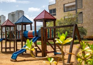 A playground with slides and climbing structures, set against a backdrop of residential buildings. - Ocean Blue/ Vista y Atardeceres (Porlamar)