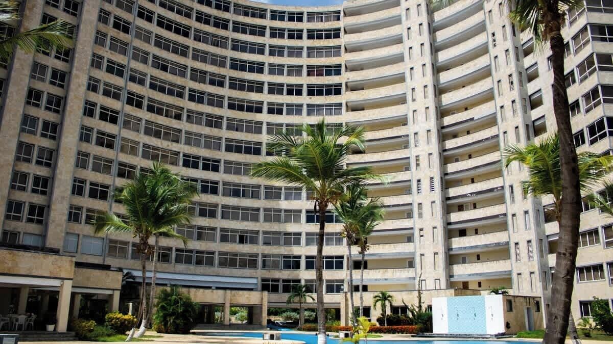 A multi-story building with a curved facade, featuring balconies and a pool area with palm trees.