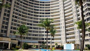 A multi-story building with a curved facade, featuring balconies and a pool area with palm trees.