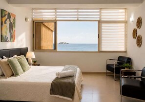 Habitación de hotel con cama, escritorio, silla, ventana con vista al mar y un cuadro en la pared.