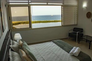Ein Hotelzimmer mit Bett, Schreibtisch, Stuhl, Fenster mit Meerblick und einer Lampe.