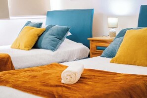 A hotel room with two beds, each with a blue headboard, a wooden nightstand with a lamp, and a rolled towel on the bed. - Ocean Blue/ Vista y Atardeceres (Porlamar)