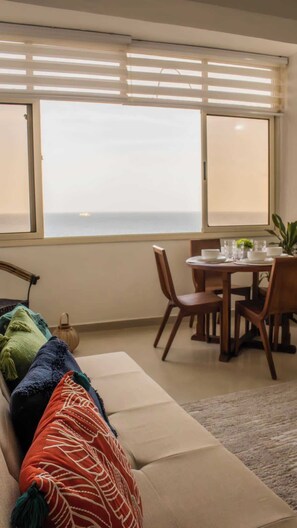 Um quarto com sofá, uma mesa de jantar com cadeiras e vista por grandes janelas.