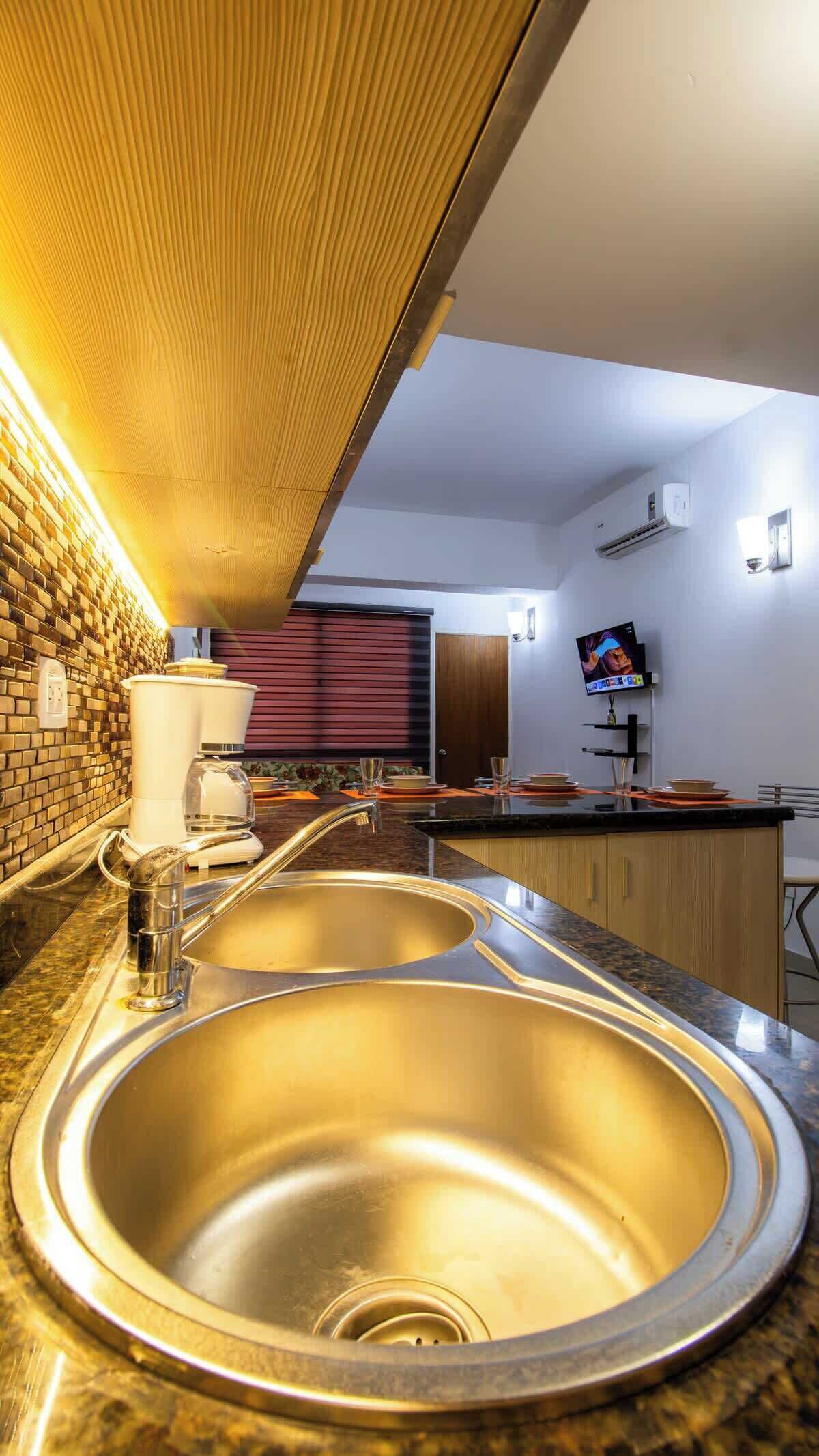 Una cucina moderna con lavello in acciaio inossidabile, macchina del caffè e televisore a parete.