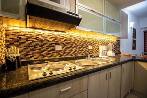 A modern kitchen with a black countertop, stainless steel appliances, and a mosaic backsplash. - Ocean Blue: Tu Refugio en Margarita (Porlamar)