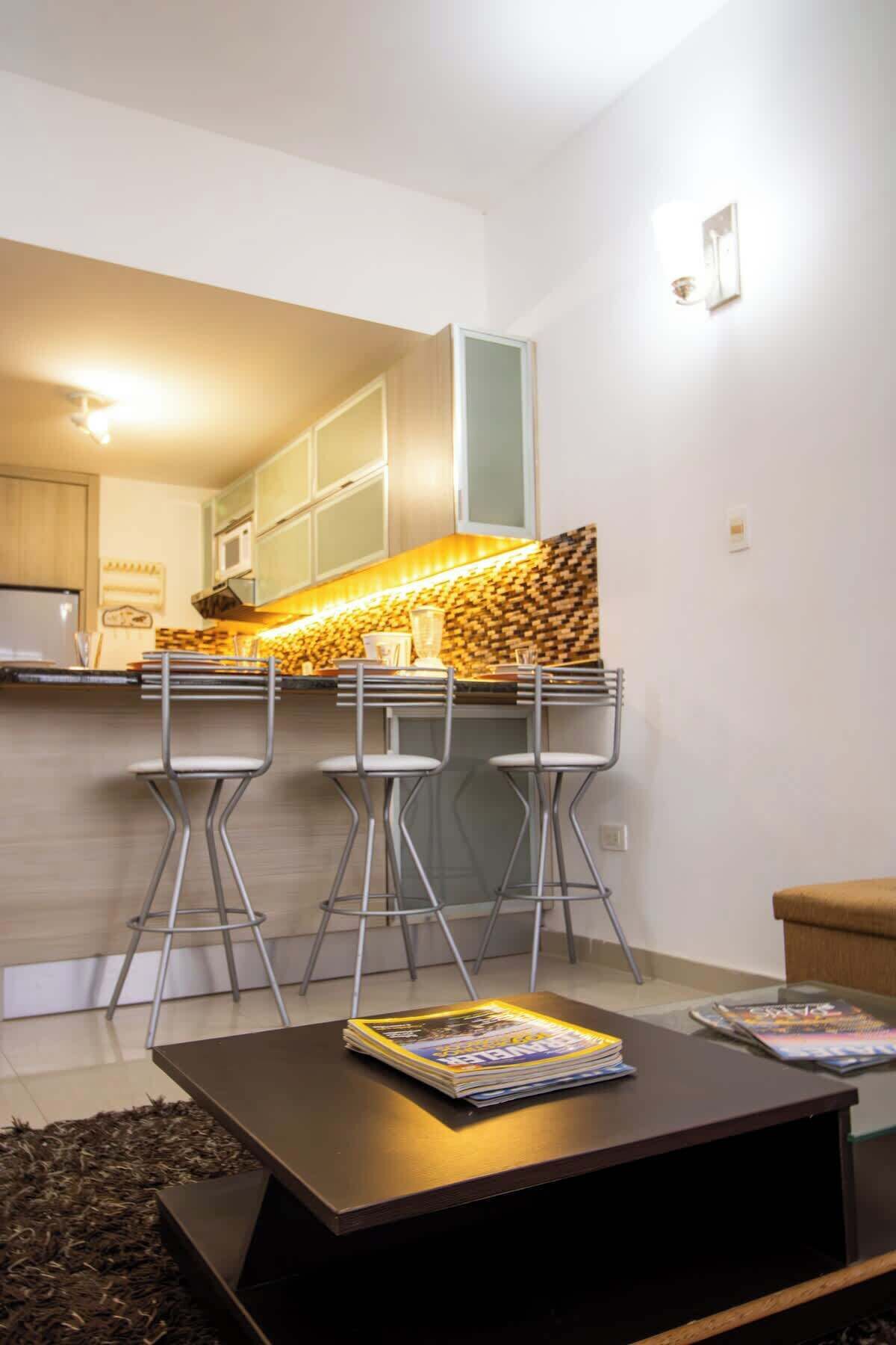 Una cucina moderna con forno a microonde integrato, un piano di lavoro in legno e una zona bar con sgabelli.