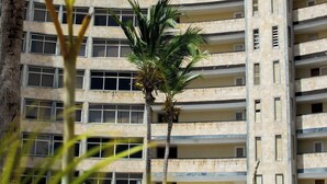 Een hoog appartementencomplex met meerdere balkons en een zwembad op de voorgrond.