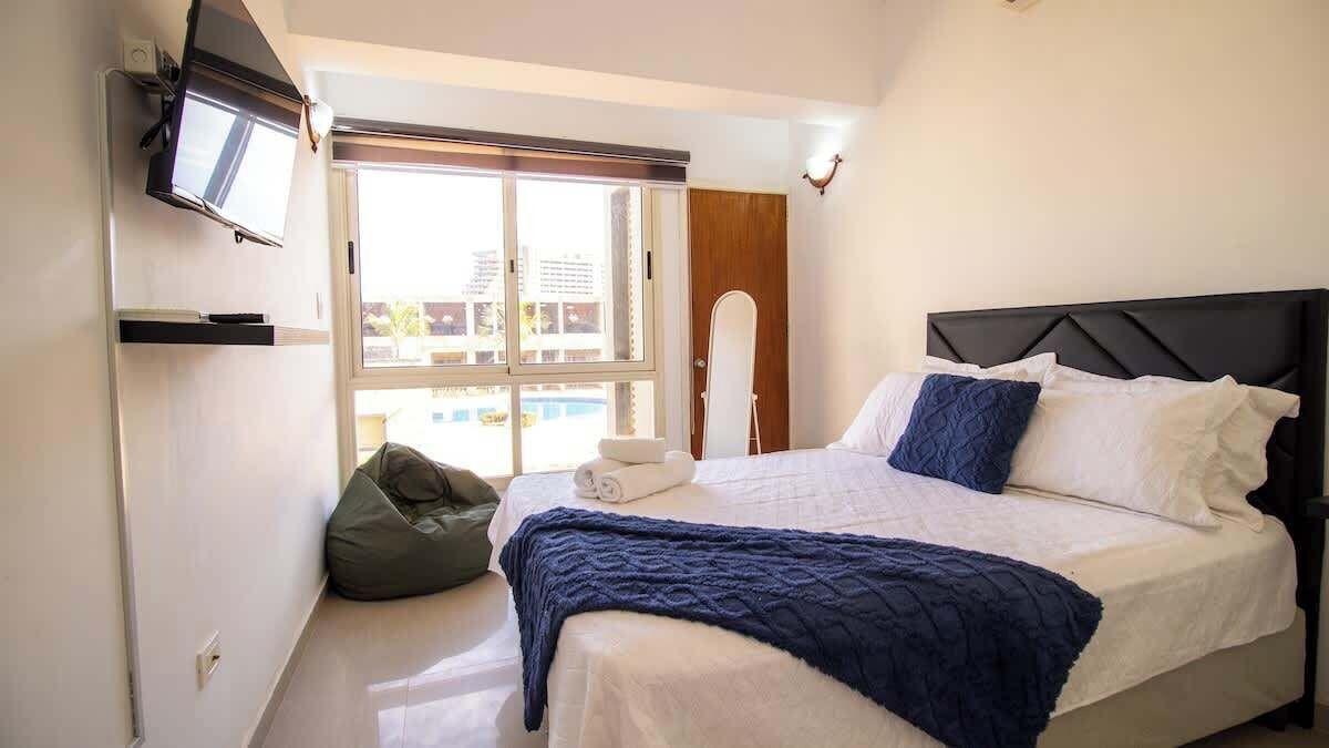 Una camera da letto con un letto, una televisione a muro, una finestra e una porta.