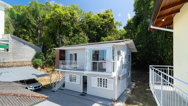 Ein zweistöckiges Haus mit Balkon, einem geparkten Auto davor und einem Garten.