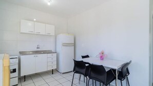 Eine kompakte Küche mit weißen Schränken, einem weißen Kühlschrank, einem kleinen Backofen und einem Esstisch mit vier Stühlen.
