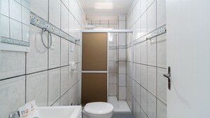 Ein schmales Badezimmer mit weißen Fliesen, Toilette, Waschbecken und Duschbereich.