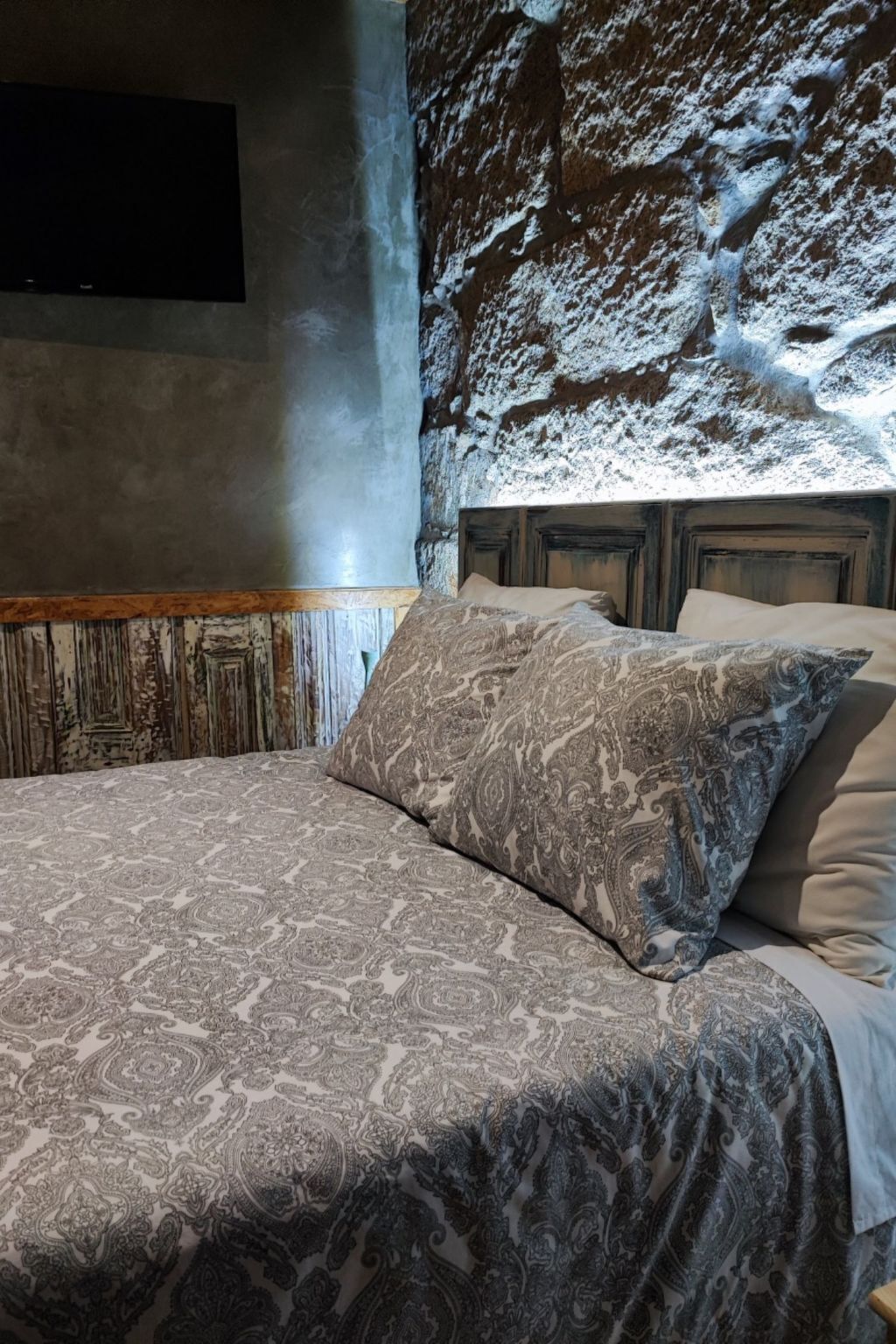 Un lit avec une literie à motifs, une tête de lit en bois et un mur à la texture particulière.