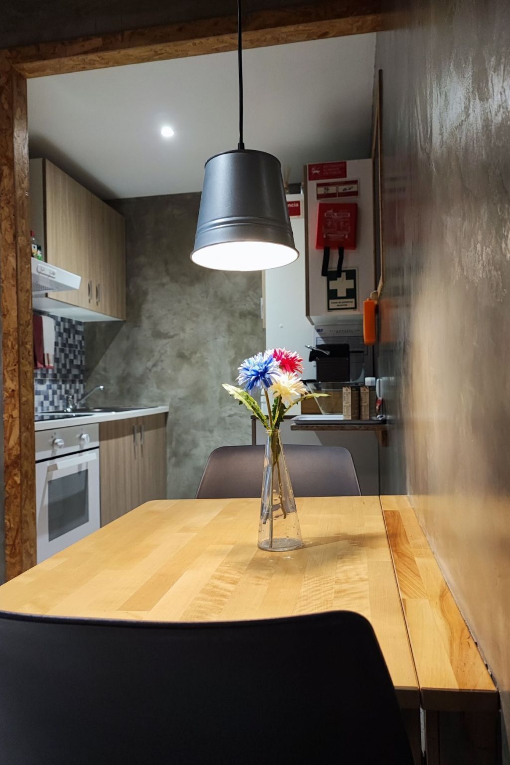 A dining area with a wooden table, a vase with flowers, and a hanging light fixture.