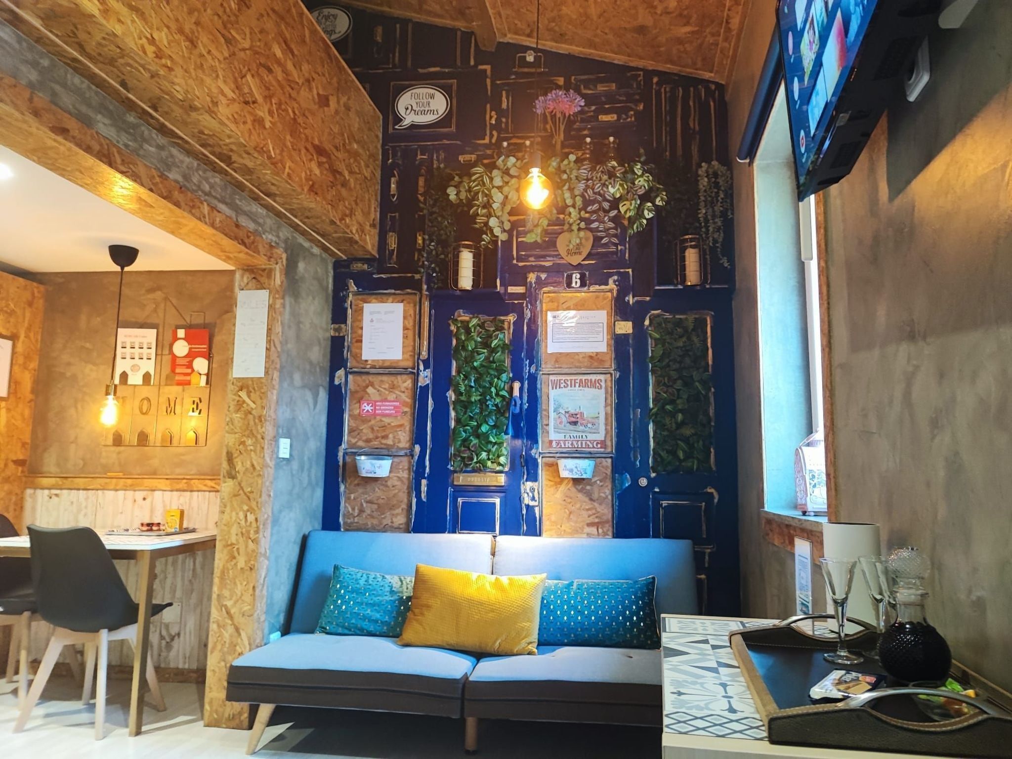 Een gezellige kamer met een blauwe bank, houten plafond en een wand versierd met diverse decoraties en planten.
