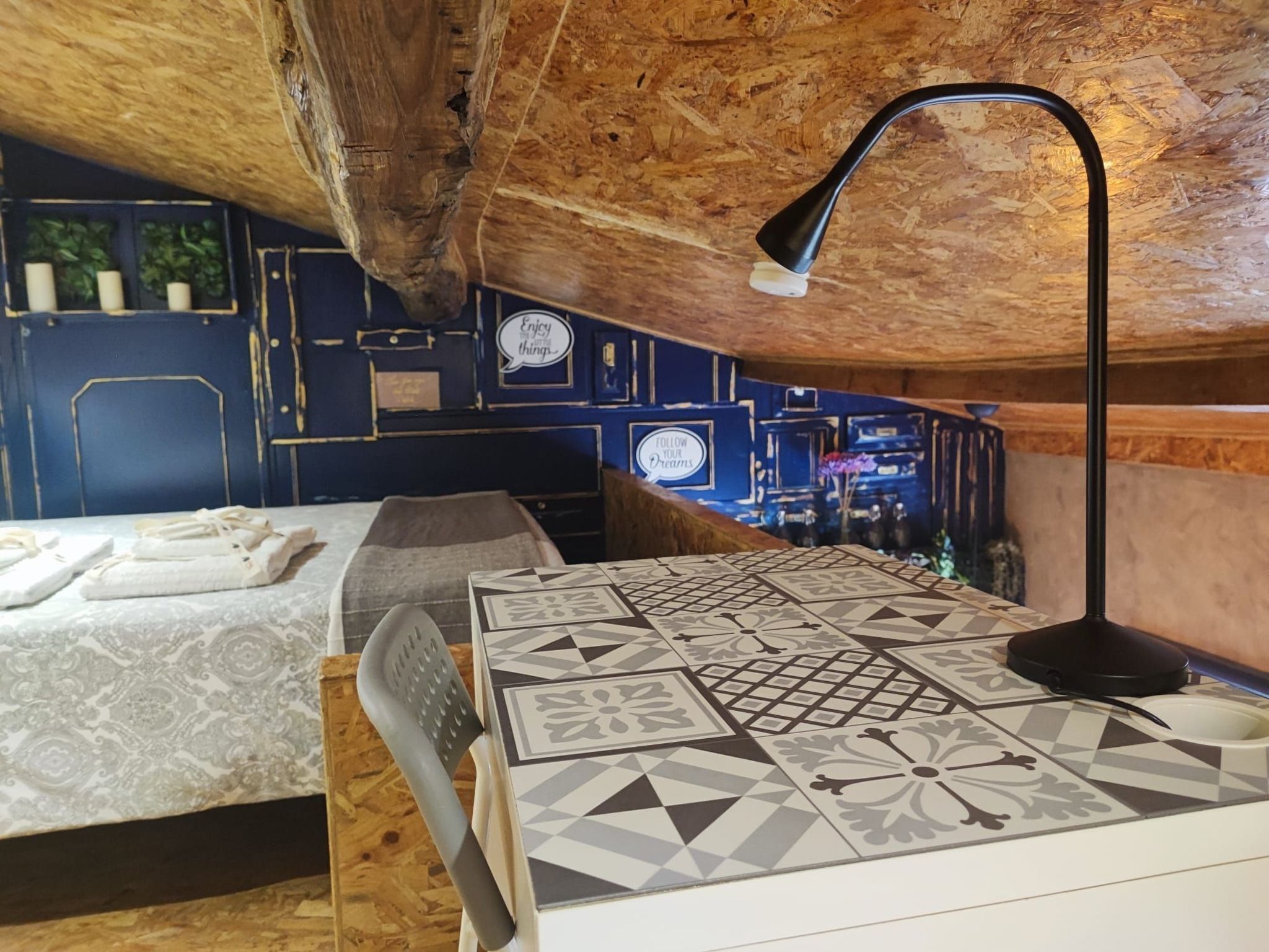 Una camera accogliente con soffitto spiovente, un letto con copripiumino fantasia, una scrivania con lampada e un muro decorato con citazioni motivazionali.