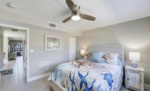 Ein Schlafzimmer mit einem Bett, einem Deckenventilator, einem Nachttisch und einer Tür zu einem anderen Raum.