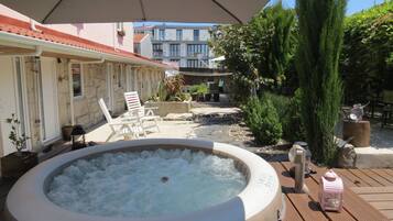 Un bain à remous dans un jardin, avec une terrasse, des chaises longues et une plateforme en bois.