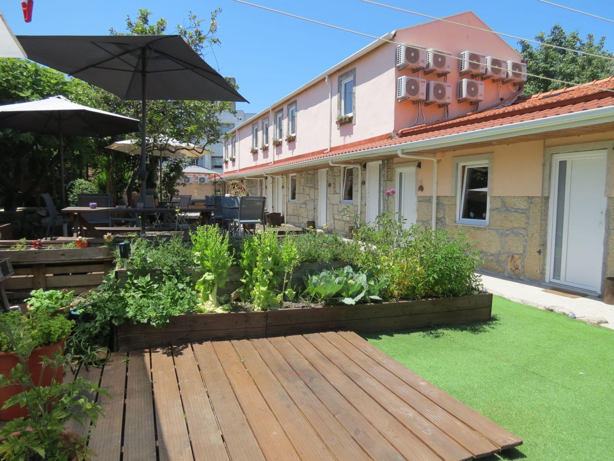 A patio area with wooden flooring, outdoor seating, and a garden bed with various plants.