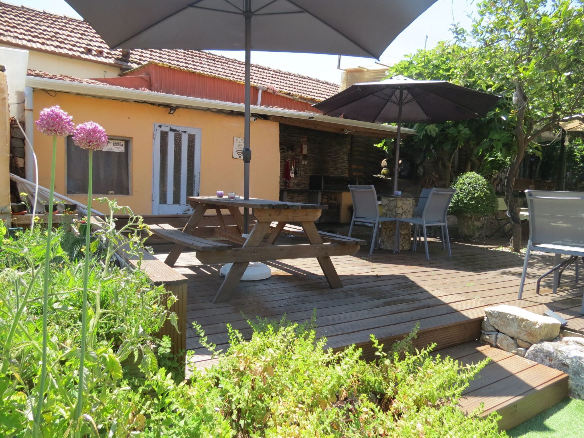 An outdoor patio area with a wooden table and chairs, a large umbrella, and a stone wall.