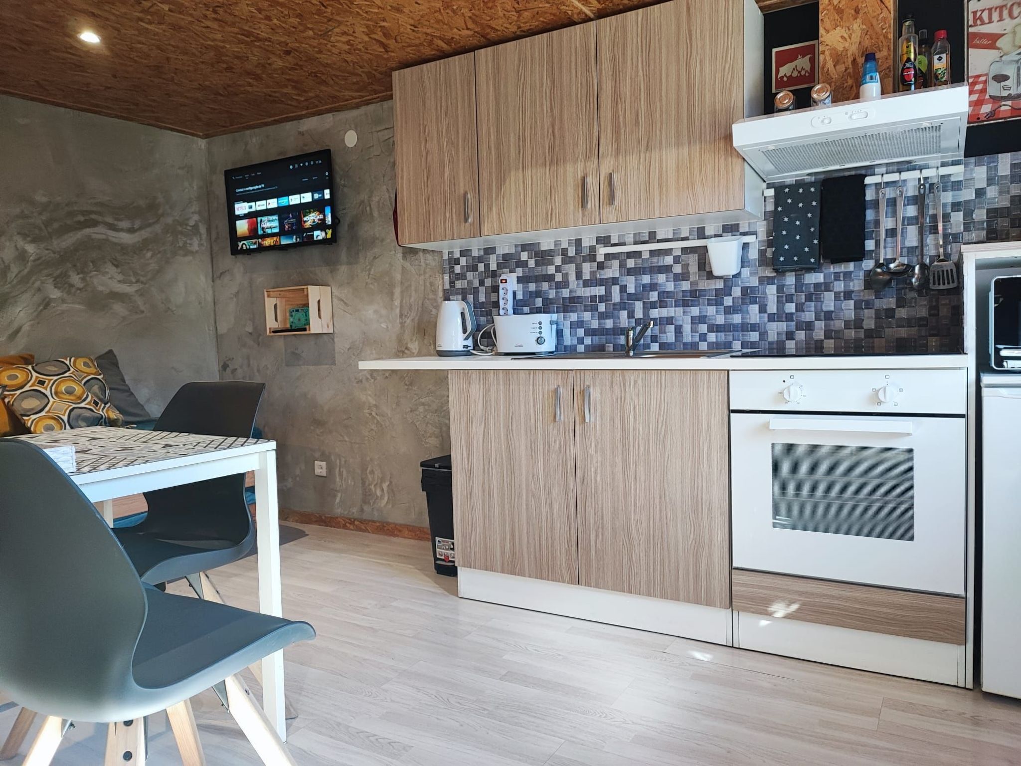 Una cucina moderna con mobili in legno, zoccolo paraschizzi in piastrelle, forno integrato e televisore a schermo piatto montato a parete.