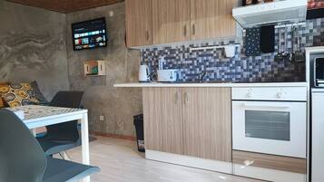 Una cucina moderna con mobili in legno, zoccolo paraschizzi in piastrelle, forno integrato e televisore a schermo piatto montato a parete.