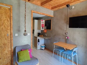 A compact living space with a kitchenette, a dining area with a table and chairs, a sofa with cushions, and a television mounted on the wall. - Rubin Charme Häuser 9 by Interhome (Porto)