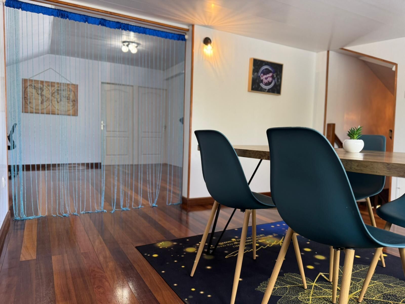 Een eetruimte met een houten tafel, twee teal stoelen, een kleine potplant en een wandlamp.