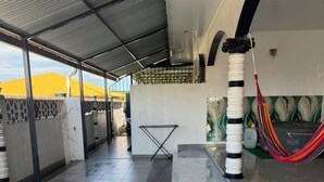 Un espacio al aire libre techado con piso de baldosas, una hamaca y una baranda de metal.