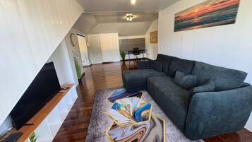 Een moderne woonkamer met een modulaire bank, een flatscreen televisie, een eethoek met tafel en stoelen, en een trap naar een hoger niveau.