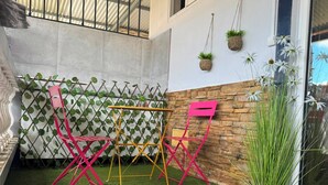 Un patio con césped artificial, una mesa, sillas y un muro decorativo con plantas.
