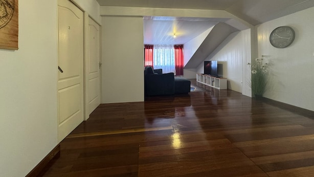 Amplia sala de estar con piso de madera, un sofá negro, un televisor y un reloj en la pared.