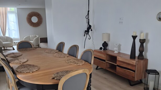 Uma sala de jantar com mesa de madeira, cadeiras estofadas cinzas e um armário de madeira com espelho.