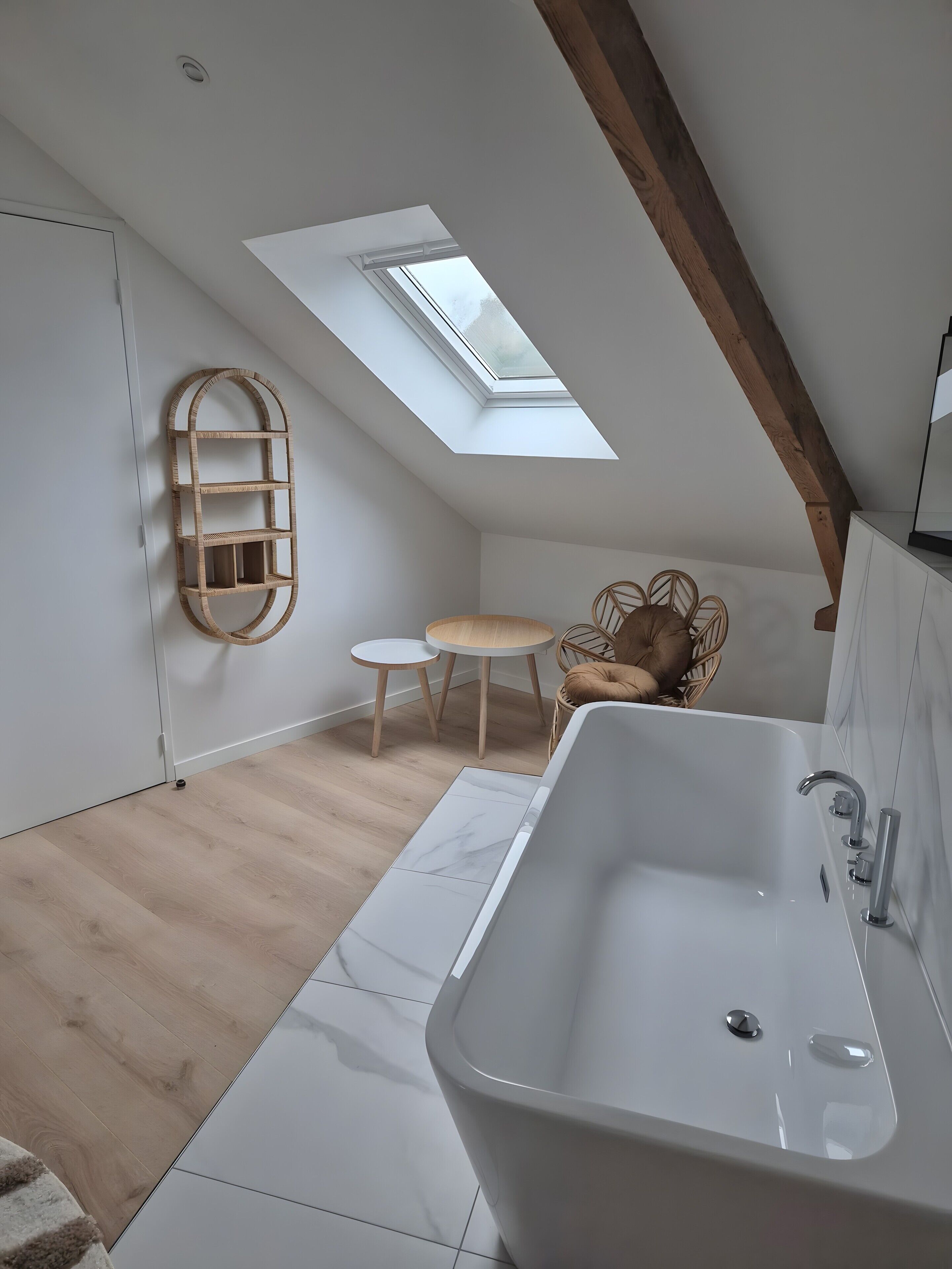 Een moderne badkamer met dakraam, een vrijstaand bad en een klein rond tafeltje met stoelen.