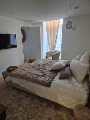 A bedroom with a large bed, a television, a chair, and a window with curtains.