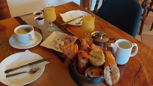 Mesa de café da manhã com croissants, doces, uma cafeteira e dois copos de suco de laranja.