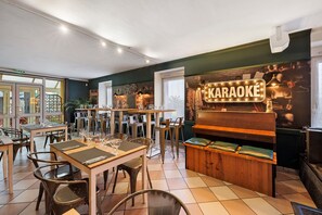 A karaoke bar with tables and chairs, a sign reading 'KARAOKE', and a stage with musical instruments.