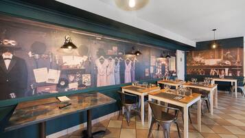 L’intérieur d’un restaurant avec des tables et des chaises en bois, et un mur décoré d’affiches et de vêtements d’époque.