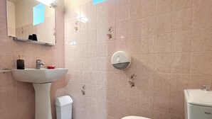 Un baño con lavamanos pedestal, inodoro, contenedor de basura y dispensador de jabón en la pared.