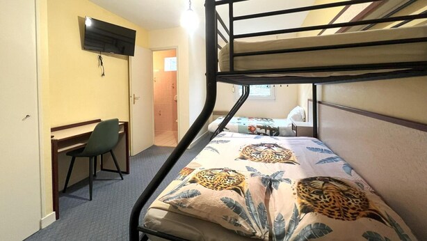 Una cama litera con un edredón estampado de leopardo, un escritorio con una silla y un televisor montado en la pared.